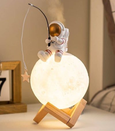 Nattlampa i form av måne med astronautfigur och glasröd fisk.