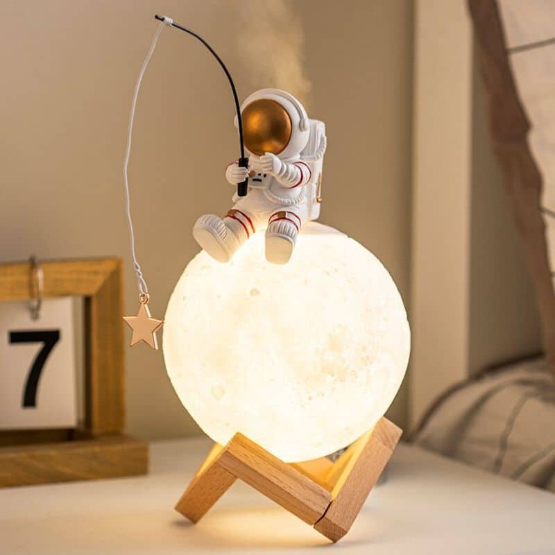 Nattlampa i form av måne med astronautfigur och glasröd fisk.