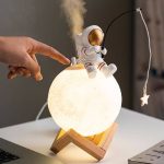 Liten astronautdekoration på en lysande måne, som lyser upp ett bord, med en neutral bakgrund, idealisk för vetenskaplig eller tematisk dekoration.