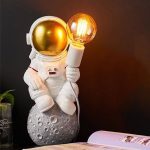 Astronautfigur i kostym med tänd LED-lampa, placerad på en yta med månliknande dekoration. Idealisk för vetenskaplig eller rymdtemat dekoration.