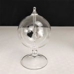 Transparent pendelboll i glas med hängande mekanism, elegant vetenskaplig dekoration, på svart och vit bakgrund.