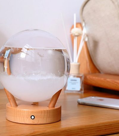 En diffusor av eteriska oljor i form av en glob, placerad på ett träbord, med en modern kontors- eller vardagsrumsinredning.