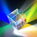 Transparent glas kub som projicerar blå, gröna, gula och rosa färgade ljus, vilket skapar ett spel av reflexer och skuggor på en mörk yta.