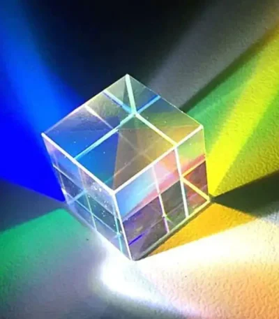 Transparent glas kub som projicerar blå, gröna, gula och rosa färgade ljus, vilket skapar ett spel av reflexer och skuggor på en mörk yta.