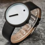 Minimalistisk klocka med vit urtavla, svarta visare och en liten svart detalj, svart silikonarmband, ren och modern design.
