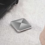 Bärbar lagringspanel i grå aluminium, kompakt och modern, placerad på en ljus tygyta, bredvid en bärbar dator.