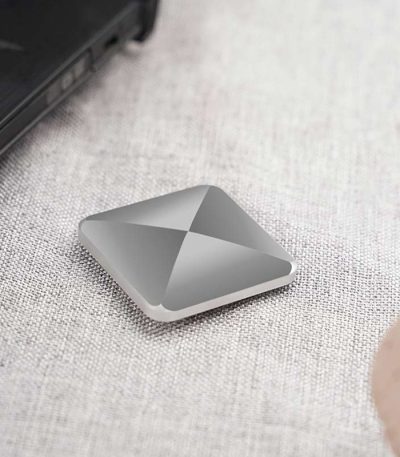 Bärbar lagringspanel i grå aluminium, kompakt och modern, placerad på en ljus tygyta, bredvid en bärbar dator.