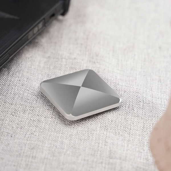 Bärbar lagringspanel i grå aluminium, kompakt och modern, placerad på en ljus tygyta, bredvid en bärbar dator.