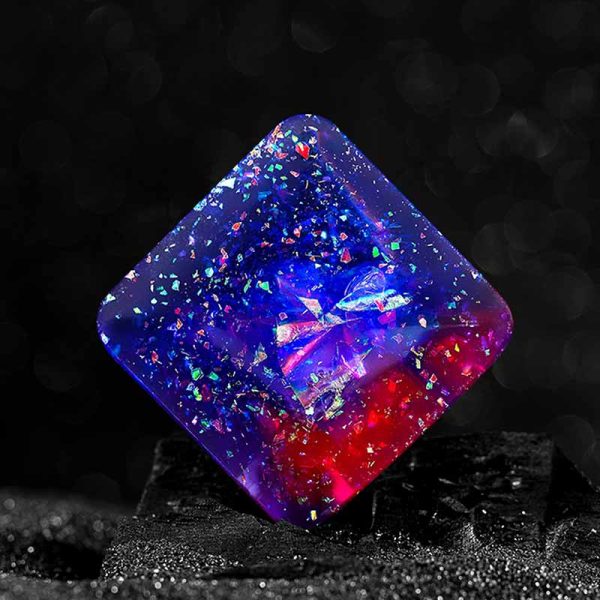 Transparent resin-kub med fluorescerande färgfläckar, belyst i mörkret, vilket skapar en fängslande och mystisk visuell effekt.
