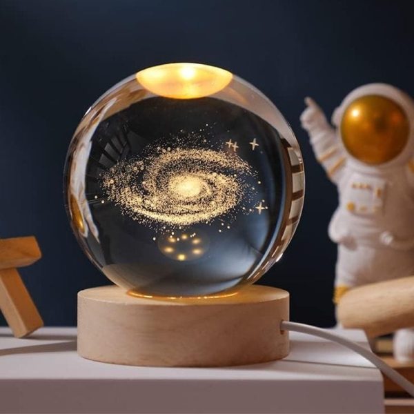 Glaskula som innehåller en miniatyrgalax med stjärnor och kosmisk damm, placerad på en träbas, idealisk för inredning med vetenskapligt eller kosmologiskt tema.