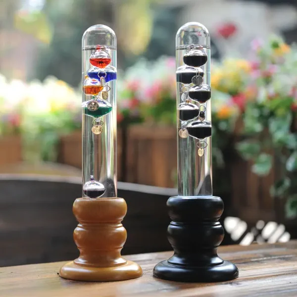 Newtonsvängning med hängande färgade kulor, som illustrerar lagen om bevarande av rörelsemängd, på ett träbord med en suddig bakgrund av blommor.