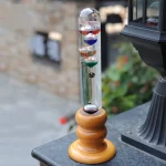 Newtonboll med färgade glaspendlar och trästöd, som illustrerar en klassisk vetenskaplig anordning för demonstration av energins bevarande.