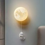 Vägglampa i form av en måne med en hängande astronautfigur, som skapar en rymdatmosfär och varm känsla i rummet.