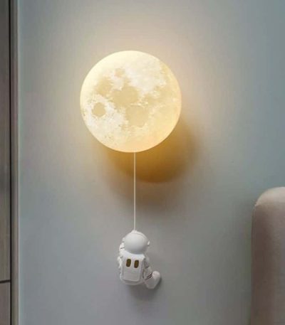 Vägglampa i form av en måne med en hängande astronautfigur, som skapar en rymdatmosfär och varm känsla i rummet.