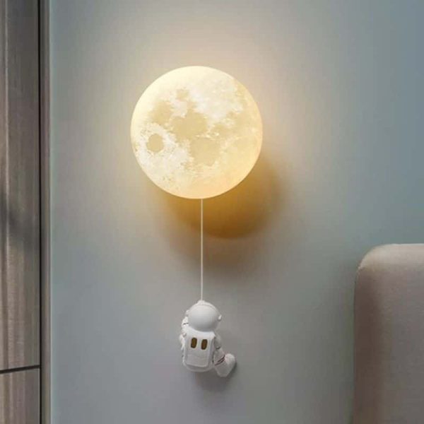 Vägglampa i form av en måne med en hängande astronautfigur, som skapar en rymdatmosfär och varm känsla i rummet.