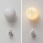 Vägglampa i form av en måne med en liten astronaut hängande, idealisk för en original och utbildande dekoration.