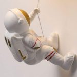 Astronautfigur i vit plast med gyllene och röda detaljer, hängande i en snöre, som väcker tankar om rymdutforskning.