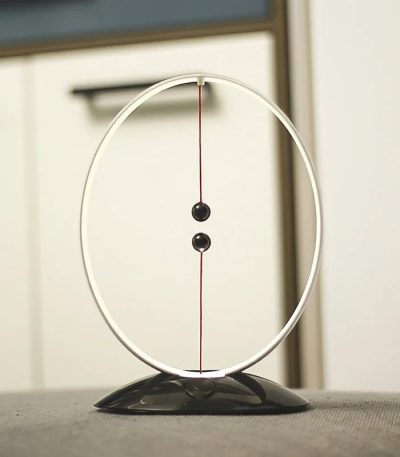 Newtonpendel i vetenskaplig inredning, som illustrerar fysik med två sfärer hängande i en cirkulär ram, perfekt för kontors- eller utbildningsinredning.