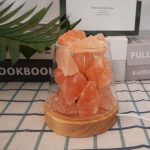 Stora rosa Himalaya saltkrystaller i en glasburk på en träbas, med en bakgrund av böcker och en grön växt.