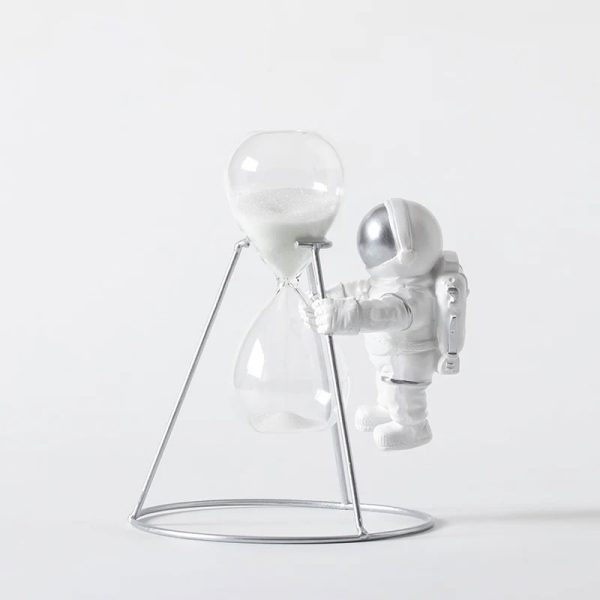Sandur i glas med metallstöd, dekoration i vetenskaplig och rymdinspirerad stil, som representerar en astronaut i vit dräkt som hanterar ett sandur.