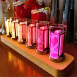 Lysande Nixie-siffror i olika färger på ett trästöd, perfekta för vetenskaplig eller vintage-dekoration.