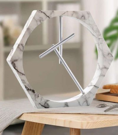 Modern klocka i hexagonform med ram i vit marmor och metallvisare, idealisk för en elegant och samtida inredning.
