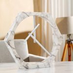 Designklocka i form av en hexagon i vit marmor med moderna metallvisare.