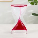 Laboratorieklocka i transparent glas med röd sand, symbol för tid och vetenskap, idealisk för dekoration eller vetenskaplig undervisning.