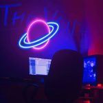 Neonljuspanel som visar en planet med ringar, i en laboratoriemiljö eller kreativt utrymme.