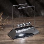 Newtonpendel i glänsande metall, dekorativt vetenskapligt objekt för kontor eller vardagsrum, som illustrerar fysikens principer med sina hängande kulor.