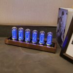 Nixie-klocka med upplysta rör som visar siffrorna 1, 2, 0, 4, 0, 4, på en träbas, dekorativ och retro, idealisk för kontors- eller vardagsrumsinredning.