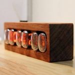 Nixie-chip i en träbox, använd som vintage-dekoration eller vetenskapligt objekt, med lysande orange siffror. Perfekt för en retro och teknologisk atmosfär.
