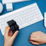 En svart Rubik's kub som hanteras av en mänsklig hand, placerad på ett vitt tangentbord, i en modern kontorsmiljö.