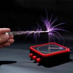 Elektrisk spole som genererar lila gnistor, placerad på en svart yta, med en hand som håller apparaten.
