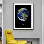 Modern affisch som representerar planeten Jorden sedd från rymden, inramad i svart, hängande på en grå vägg i en samtida inredning.