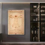 Illustration av Vitruviusmannen av Leonardo da Vinci inramad, utställd på en grå vägg, bredvid en svart hylla med porslin och dekorativa föremål.