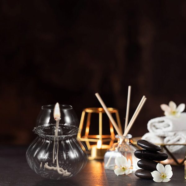 Flytande ljus i glas med tänd låga, zen-dekor med svarta stenar och vita blommor, avslappnande atmosfär för inredning eller spa.