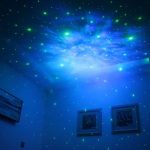 Gröna och blå fosforescerande stjärnor projicerade på taket och väggarna i ett mörkt rum, vilket skapar en kosmisk och avslappnande atmosfär.