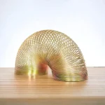 Guld spiralformad skulptur i metall, modern och konstnärlig design, placerad på en ljus träyta, idealisk för vetenskaplig eller samtida dekoration.