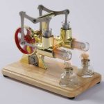 Vintage laboratoriemodell av ångmaskin med glasrör och metallmekanism, placerad på en träbas, som illustrerar ett dekorativt vetenskapligt objekt.