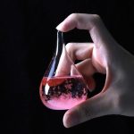 Laboratoriepipett som innehåller en bubblande rosa vätska, hålls av en mänsklig hand, mot svart bakgrund. Idealisk för vetenskaplig eller utbildningsdekoration.