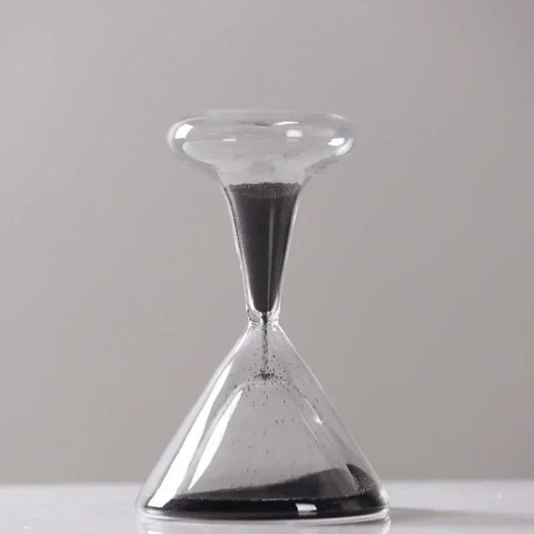 Laboratoriesandur med svart sand, symbol för tid och vetenskap, i transparent glas, placerad på en vit yta, som illustrerar tidens mätning i ett vetenskapligt sammanhang.