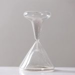 Transparent sandur i glas med fin vit sand, symbol för den passerande tiden, placerad på en vit yta med en ljusgrå bakgrund.