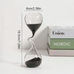Dekorativt sandur i glas med svart sand, som mäter 18,5 cm i höjd och 6 cm i bredd, idealiskt för inredning eller som samlarobjekt.