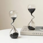 Dekorativt sandur i glas med svart sand och spiral, idealiskt för vetenskaplig eller modern dekoration. Elegant och originaldesign, perfekt för ett skrivbord eller en samtida inredning.