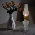 Njut av den varma atmosfären med denna bild av en keramikvas med gula blommor, tillsammans med en tänd gammal oljelampa, som skapar en mysig och retro stämning.