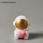 Astronautdocka i vit keramik, med gyllene ansikte och rosa hjärta, idealisk för vetenskaplig dekoration eller som en originell present.