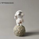 Astronautfigur i dekoration, som föreställer en kosmonaut i rymddräkt på en månlandskap, idealisk för tematisk vetenskaplig dekoration.