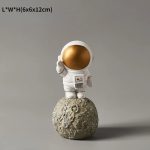 Vit plastastronautfigur med glänsande gyllene hjälm, placerad på en liten stenmåne.