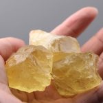 Genomskinlig gul resin-kristall, rå och naturlig, hålls mellan fingrarna. Perfekt för dekoration eller insamling av vetenskapliga objekt.